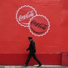 A security guard walks past Coca-Cola advertisement in Mexico City on October 17, 2025. US giant Coca-Cola will reduce the sugar content of its soft drinks for the Mexican market by 30% after negotiating a new tax reduction on other products in its portfolio, the government of President Claudia Sheinbaum announced this Friday. (Photo by Yuri CORTEZ / AFP)