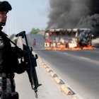 A member of the Prosecutor's Office stands guard near a burning bus at one of the main avenues after it was set on fire by organised crime groups in response to an operation in Jalisco to arrest a high-priority security target in Zapopan, state of Jalisco, Mexico, on February 22, 2026. Armed civilians blocked several roads in the state of Jalisco, in western Mexico, following an operation by federal forces in the town of Tapalpa, local authorities reported. Jalisco, which will host four matches of the upcoming 2026 World Cup, is home to the powerful Jalisco New Generation Cartel (CJNG), and has been rocked by several episodes of violence in recent years. (Photo by Ulises Ruiz / AFP)