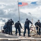 Marineros estadounidenses lanzan el cabo de amarre en la cubierta de vuelo del destructor lanzamisiles guiados de la clase Arleigh Burke USS Bainbridge (DDG 96) durante una maniobra de fondeo, el 31 de marzo de 2026.