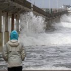 Una mujer observa cómo grandes olas rompen en la playa (Archivo)