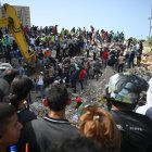 Rescatistas, voluntarios y residentes se congregan alrededor de una excavadora mientras buscan entre los escombros de los edificios derrumbados en Catia La Mar, La Guaira
