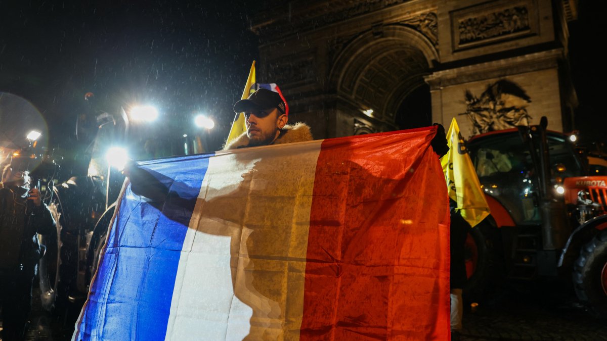 A farmer holds a French flag in front of the Arc de Triomphe.