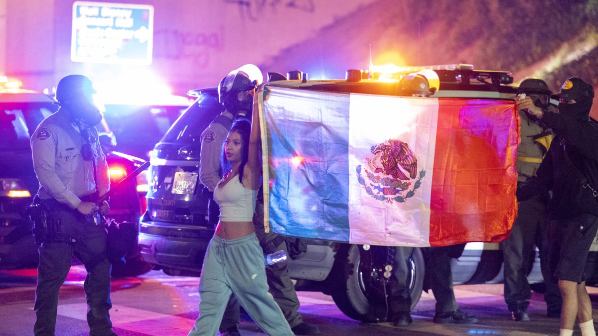 Protesters walk past sheriff's deputies with Mexican flag.