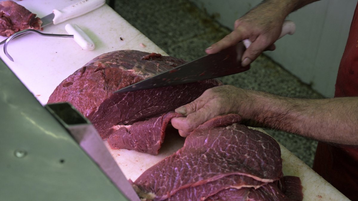 Un carnicero corta un trozo de carne-Imagen de archivo