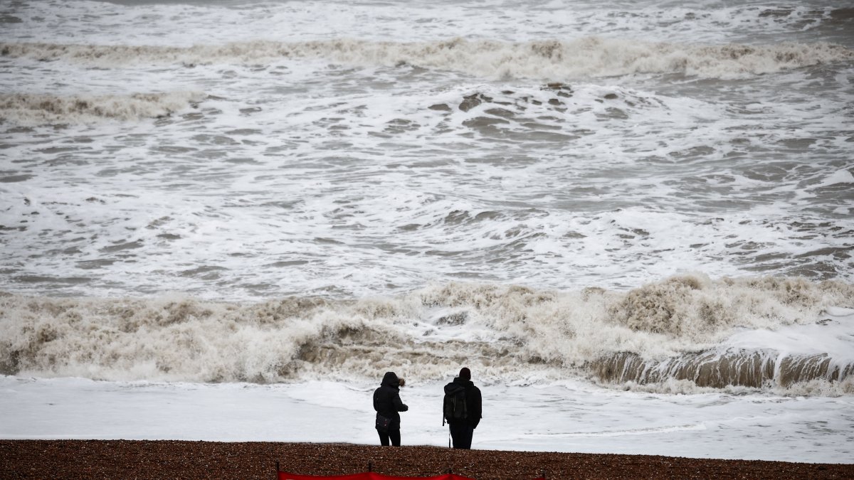 People look at the waves while standing behind a warning sign reading 