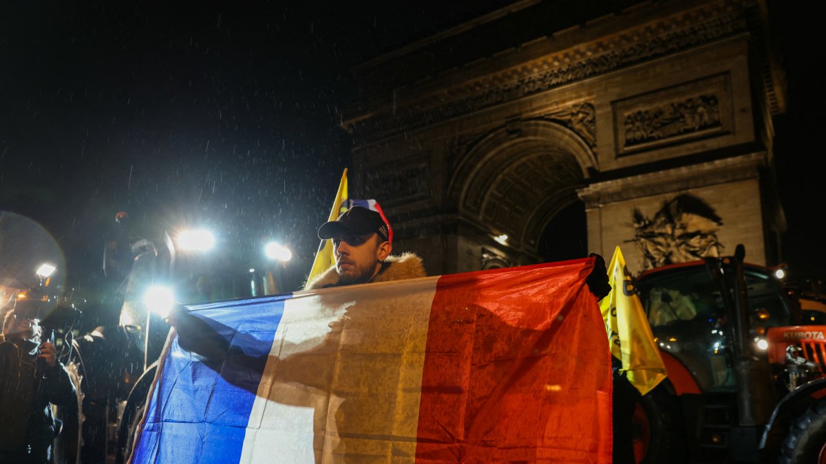 Un agricultor sostiene una bandera francesa frente al Arco del Triunfo.