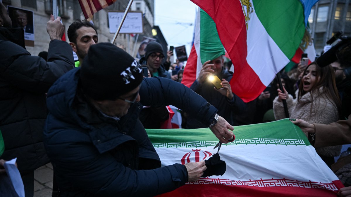 A protester cuts the flag of the Islamic Republic of Iran