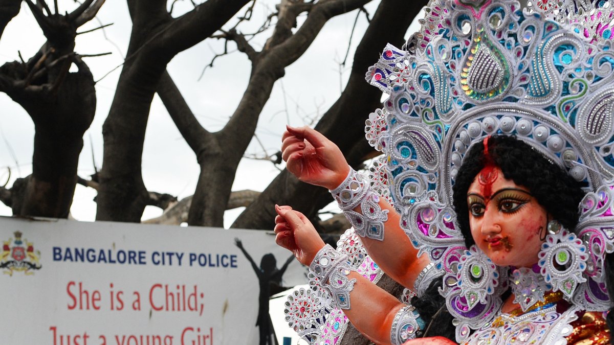 A procession passes by a banner put up against sexual exploitation and violence against girls