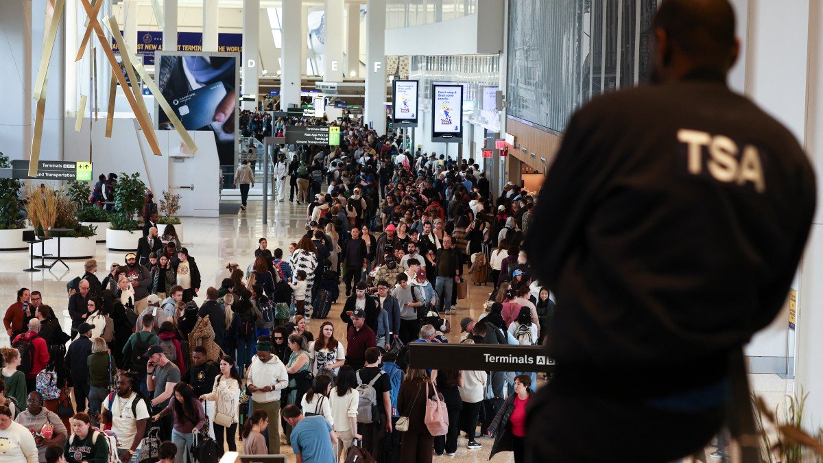 A TSA agent watches passengers lining up to go through security screening