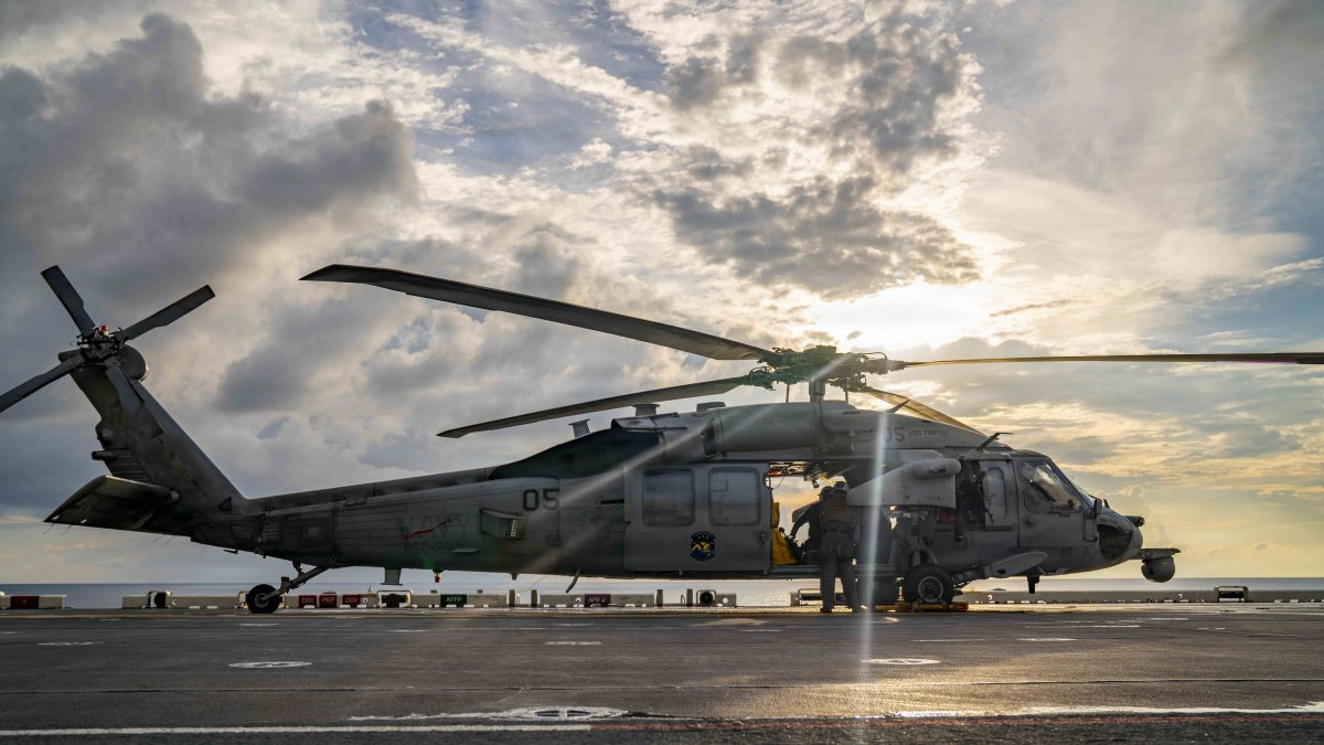 Sailors perform maintenance on a helicopter on the deck of the USS Tripoli.