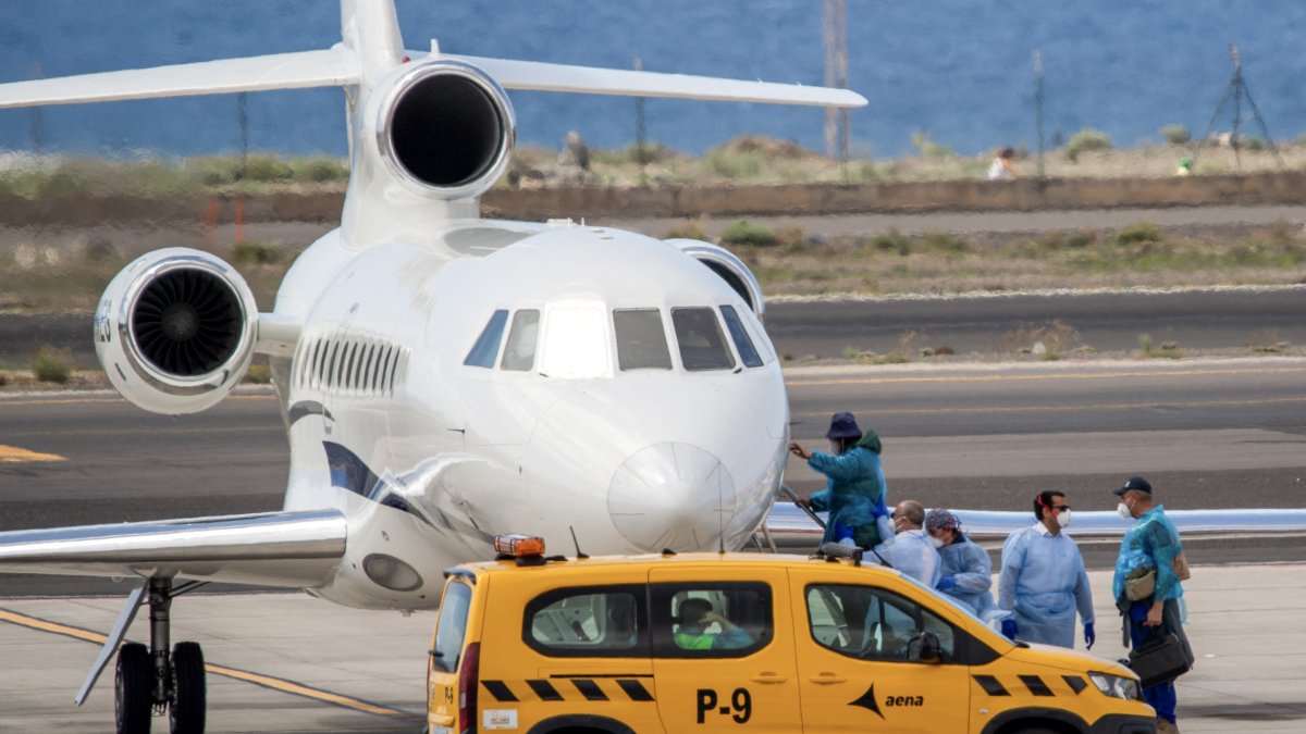 Pasajeros con trajes protectores azules abordan un avión tras ser evacuados del crucero MV Hondius