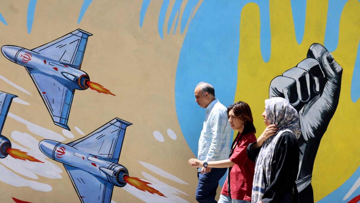 Iranian citizens walk past an anti-U.S. and anti-Israeli mural painted on a wall in the capital Tehran on May 10, 2026.