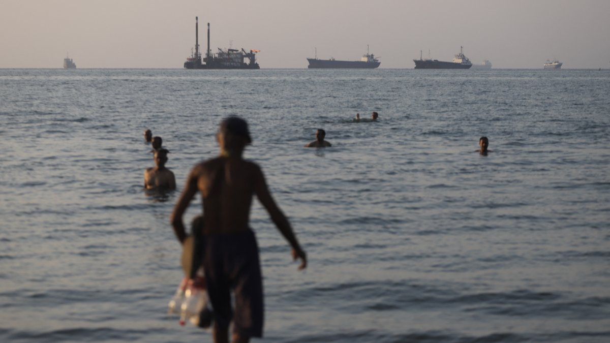 Cargo and commercial vessels anchored in the Strait of Hormuz, while residents of Bandar Abbas enjoy themselves in the water.