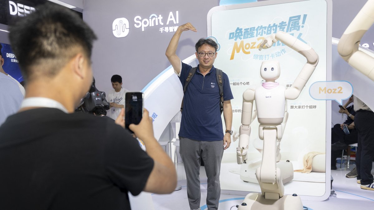 A visitor and a humanoid robot make heart gestures while posing for photos during the 2026 World AI Conference in Shanghai.