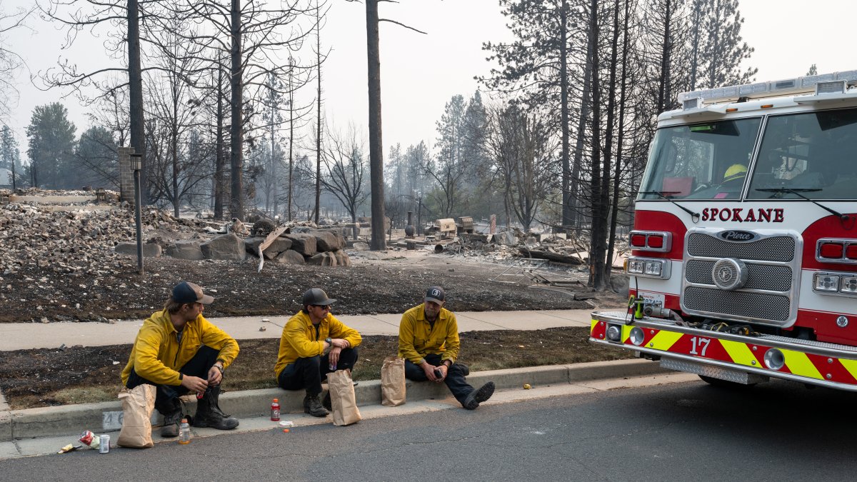 Tres bomberos realizan una pausa para comer entre las ruinas de Spokane