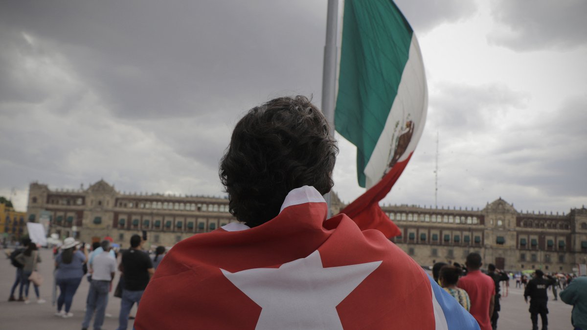 Una persona con una bandera cubana frente a la bandera de México (Archivo)
