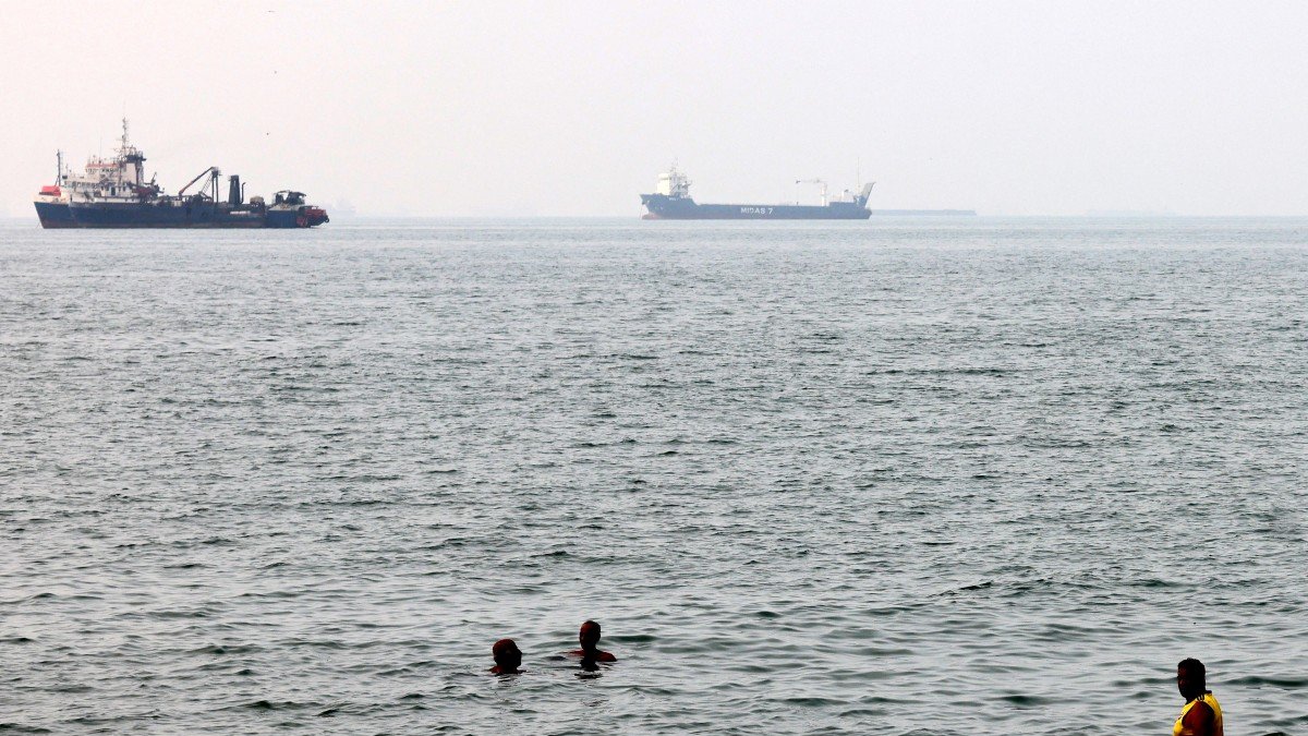 Unos hombres se bañan en las aguas del Golfo mientras varias embarcaciones atraviesan el estrecho de Ormuz