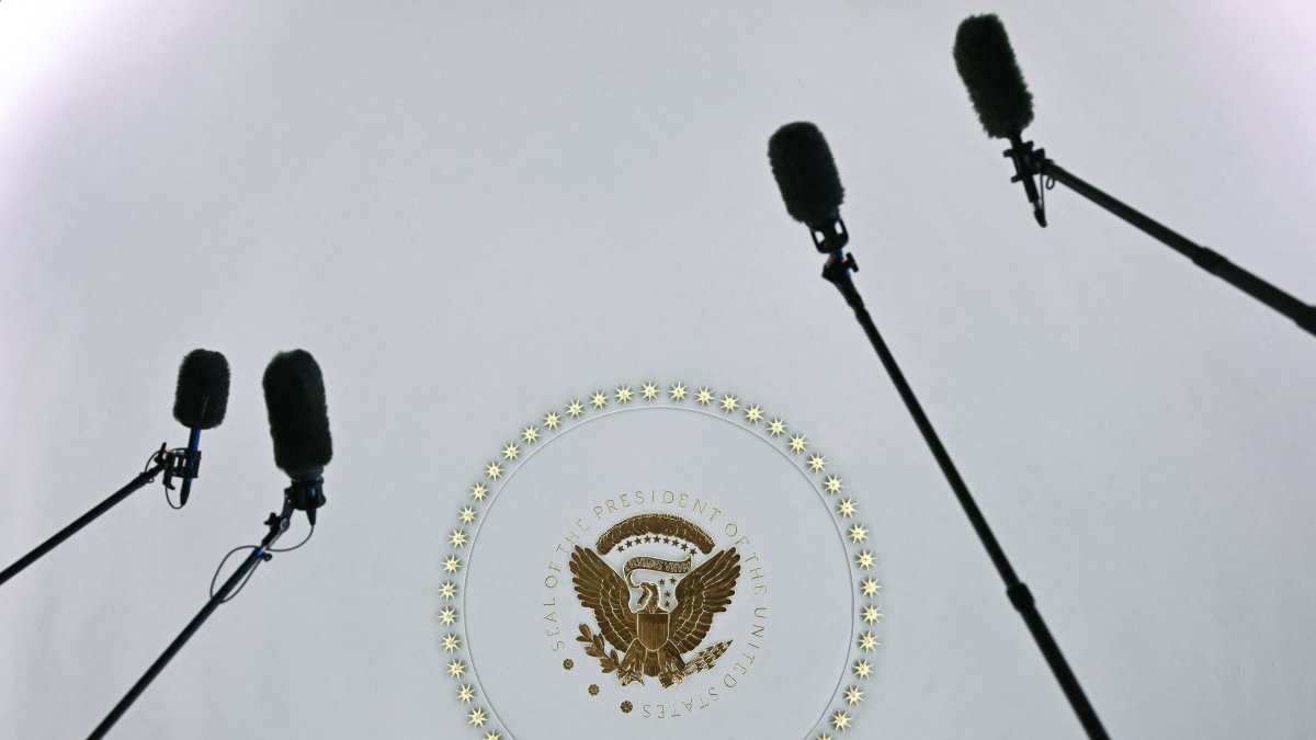 Journalists hold microphones as the presidential seal and a circle of stars on the ceiling are seen.