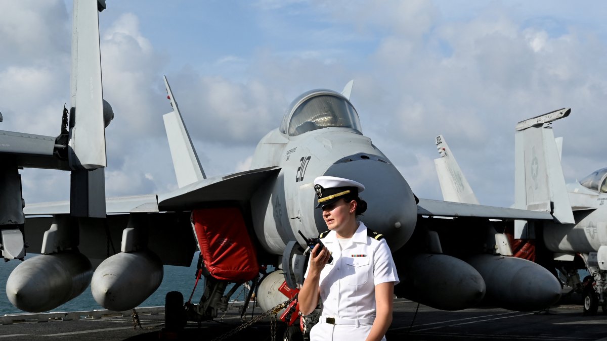 A U.S. Navy sailor stands next to an aircraft on the deck of the aircraft carrier USS George Washington.