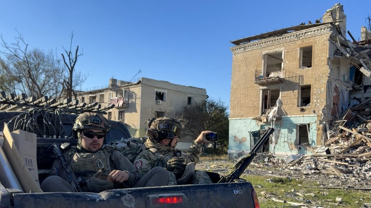 Ukrainian soldiers drive past damaged buildings in a pickup truck