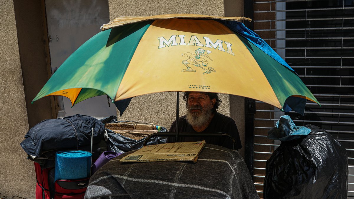 A homeless person sits in the shade of a beach umbrella during a heat wave in Miami