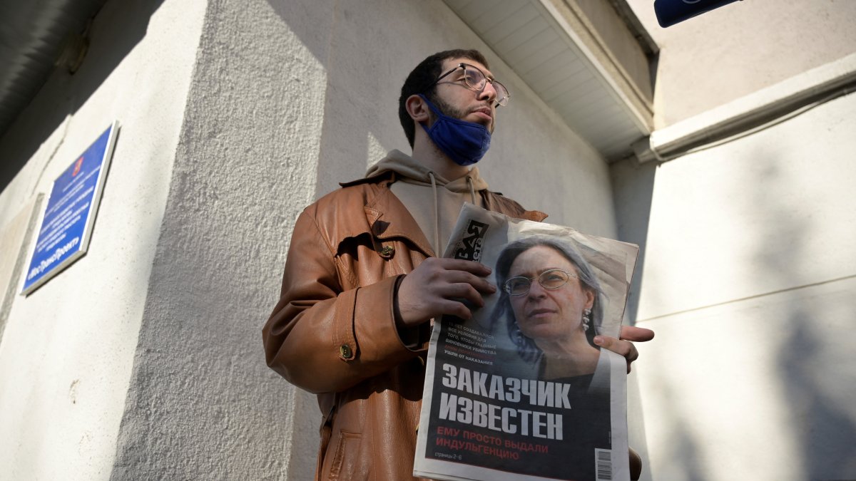 A man is holding a newspaper featuring a photo of investigative journalist Anna Politkovskaya