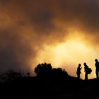 Varios bomberos observan cómo el fuego asciende por las colinas detrás de Pacific Palisades el sábado por la mañana mientras los aviones de extinción de incendios lanzan agua y rellenan para combatir las llamas