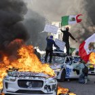 Manifestantes ondean banderas desde lo alto de un coche destrozado, junto a vehículos Waymo en llamas, mientras los manifestantes se enfrentan a las fuerzas del orden en las calles que rodean el edificio federal durante una protesta tras las operaciones federales de inmigración en Los Ángeles, California, el 8 de junio de 2025. Manifestantes incendiaron coches y se enfrentaron a las fuerzas de seguridad en Los Ángeles el 8 de junio, mientras la policía mantenía a los manifestantes alejados de las tropas de la Guardia Nacional que el presidente Donald Trump envió a las calles de la segunda ciudad más grande de EE.UU.(Foto de RINGO CHIU / AFP)