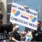 Un hombre en una marcha sostiene un cartel que reza "los niños no binarios son mis héroes".