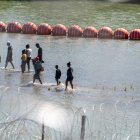 Crisis migratoria: Migrantes caminan junto a una cadena de boyas colocadas en el agua a lo largo de la frontera del Río Grande con México en Eagle Pass, Texas, el 15 de julio de 2023