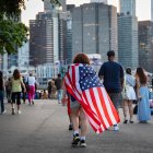 Una persona se envuelve con una bandera de Estados Unidos como una capa mientras la multitud se reúne para la celebración de los fuegos artificiales del 4 de Julio de Macy’s a lo largo del río Este