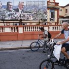 Dos hombres en Cuba transitan en bicicleta frente a una propaganda del régimen