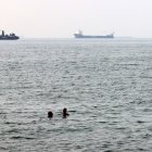 Men bathe in the Gulf waters as vessels in the background transit the Strait of Hormuz off the coast of Iran's southern port city of Bandar Abbas on September 7, 2026. Iran's top negotiator threatened on September 6 of a more forceful response to any further US attacks after Tehran targeted American warships in their latest round of clashes. The exchanges of fire, which began with US raids last week, come amid a deadlock in the six-month war between the two foes. (Photo by ATTA KENARE / AFP) /